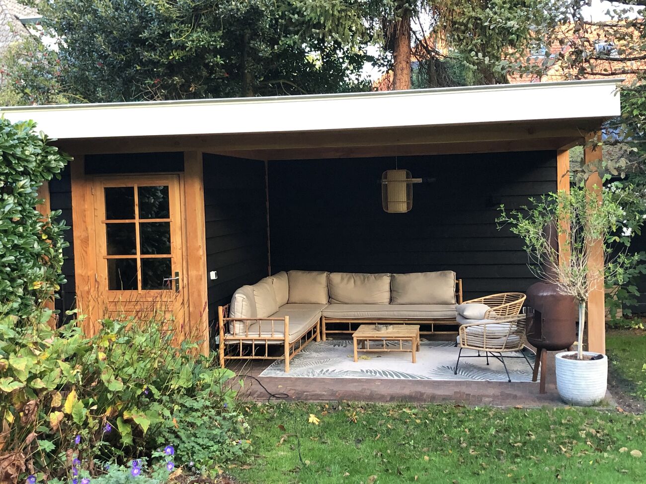 Houten overkapping in de tuin met donkere gevelbekleding en glazen deur